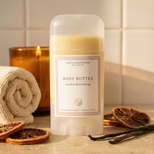 Body butter container with a label on a bathroom counter, surrounded by vanilla beans and dried oranges.