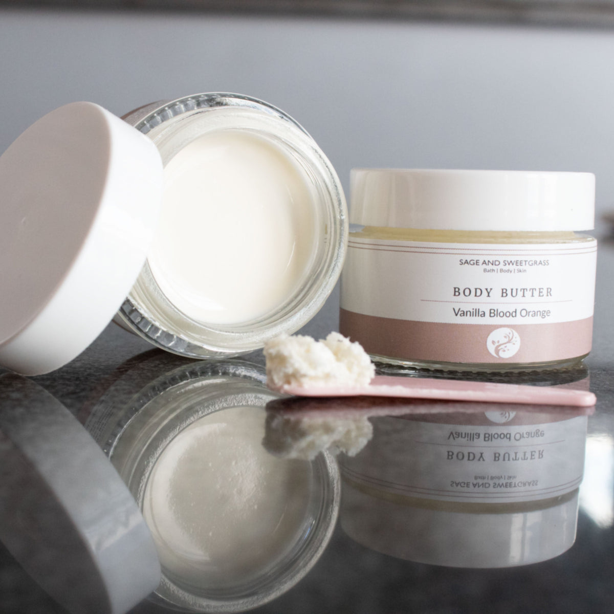 Two jars of body butter on a reflective surface with a neutral background