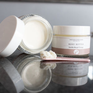 Two jars of body butter on a reflective surface with a neutral background