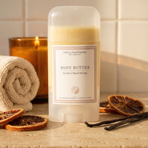 Body butter container with a label on a bathroom counter, surrounded by vanilla beans and dried oranges.
